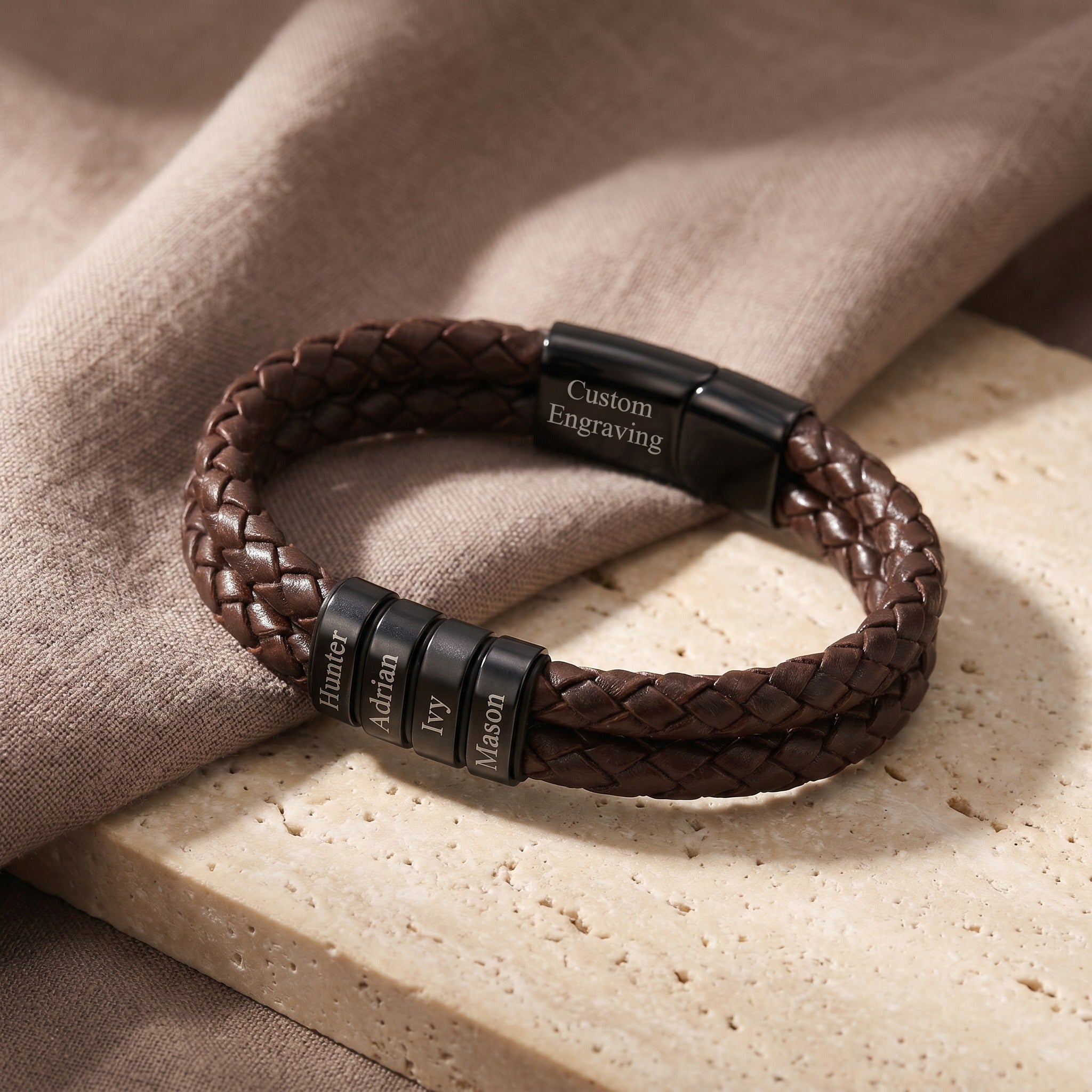 Brown braided leather bracelet with black engraved clasp on a beige surface