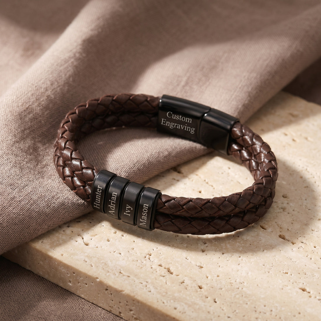 Brown braided leather bracelet with black engraved clasp on a beige surface