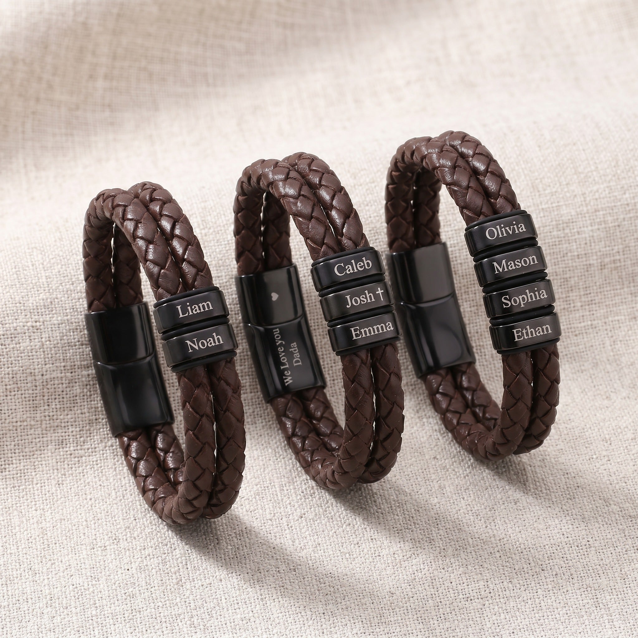 Three braided leather bracelets with engraved names on a beige fabric background