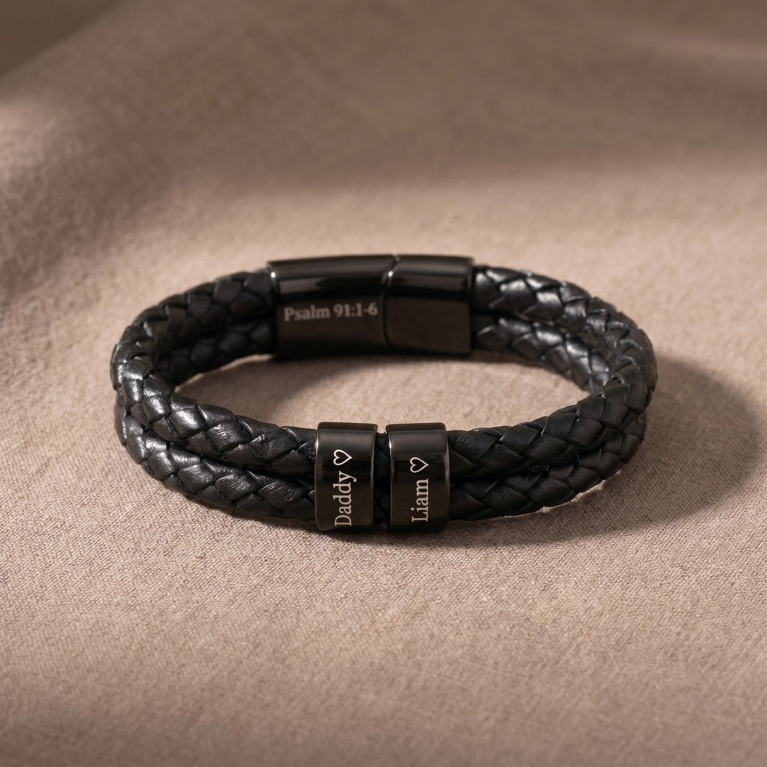 Black braided leather bracelet with engraved magnetic clasp on a beige fabric background
