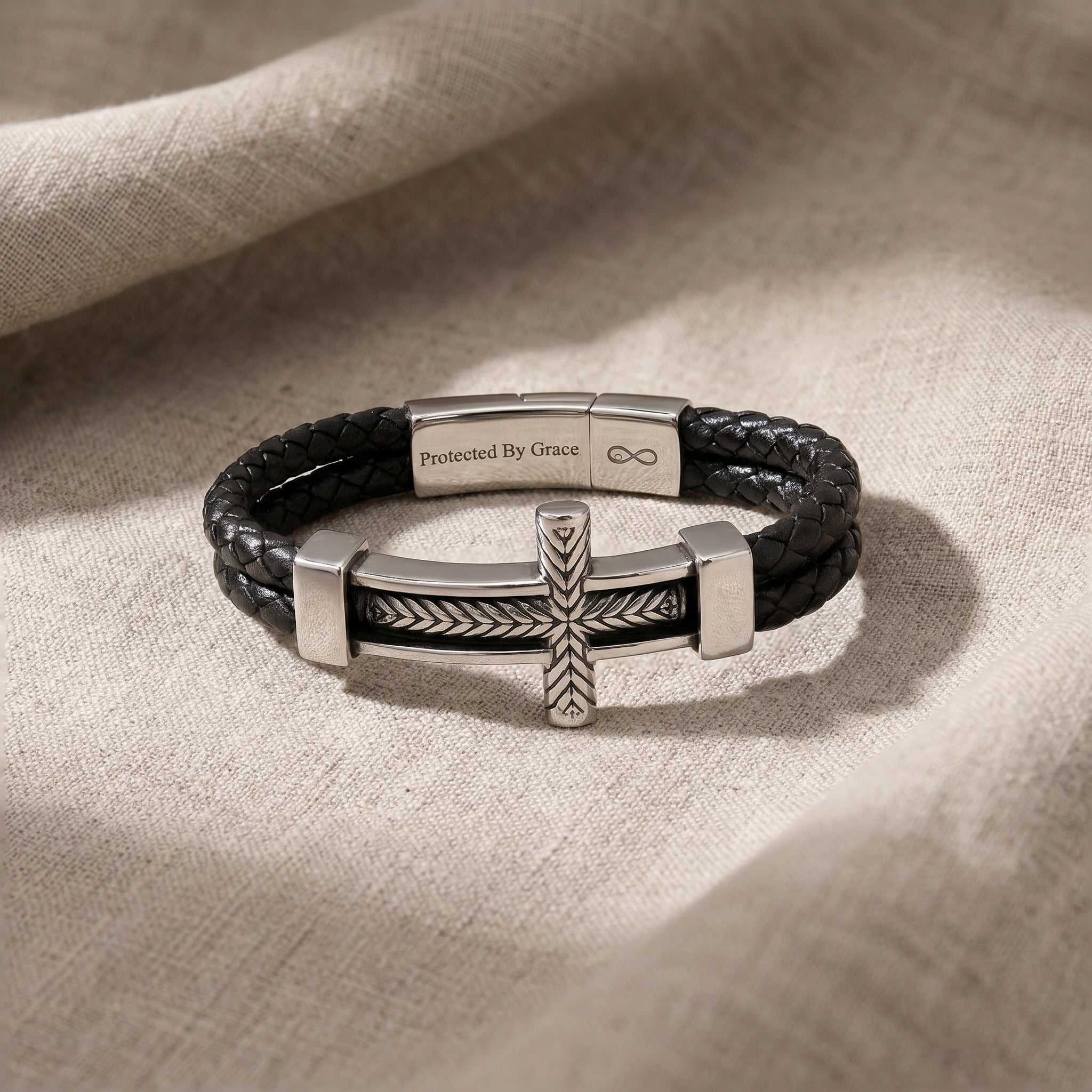 Black leather bracelet with silver cross charm on a beige fabric background