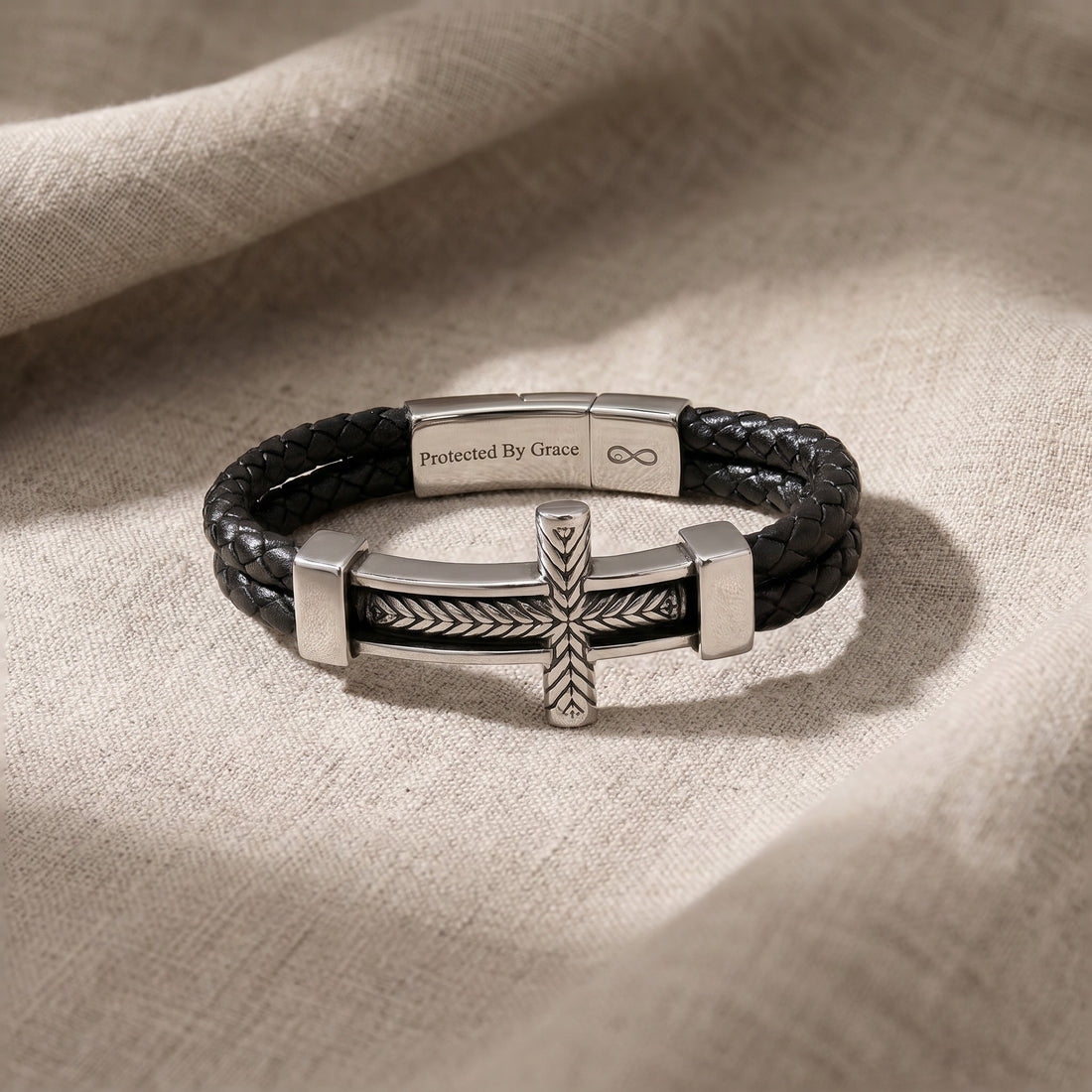 Black leather bracelet with silver cross charm on a beige fabric background