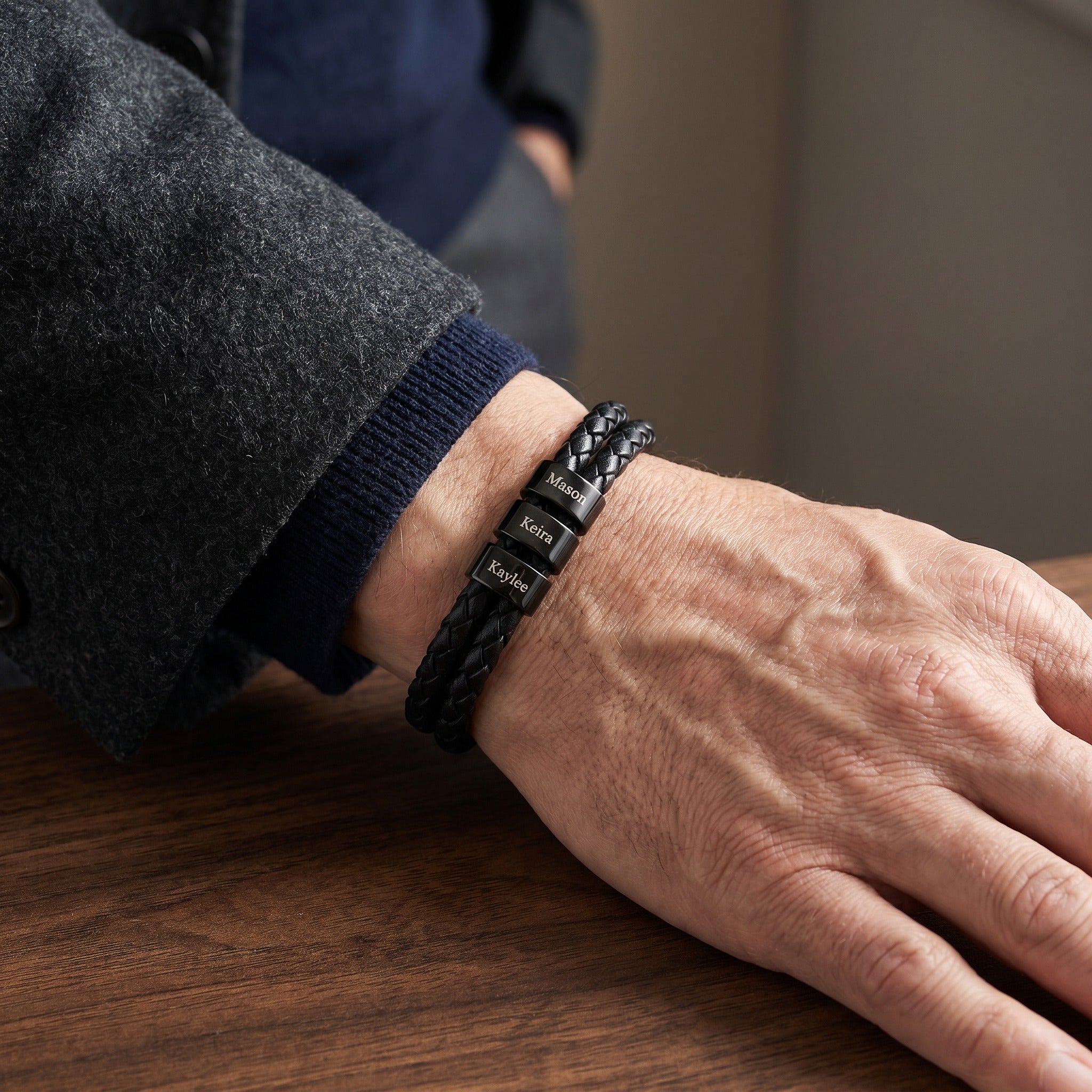 Person wearing a black leather bracelet with engraved names on a wooden surface