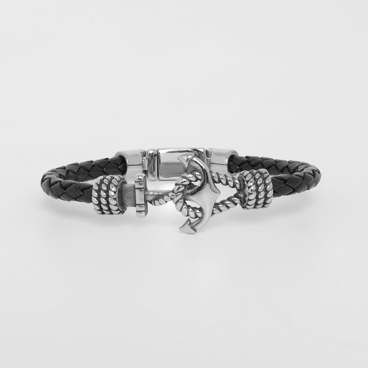 A black braided leather bracelet with a silver-toned anchor charm and textured rope details, displayed on a clean light gray background.