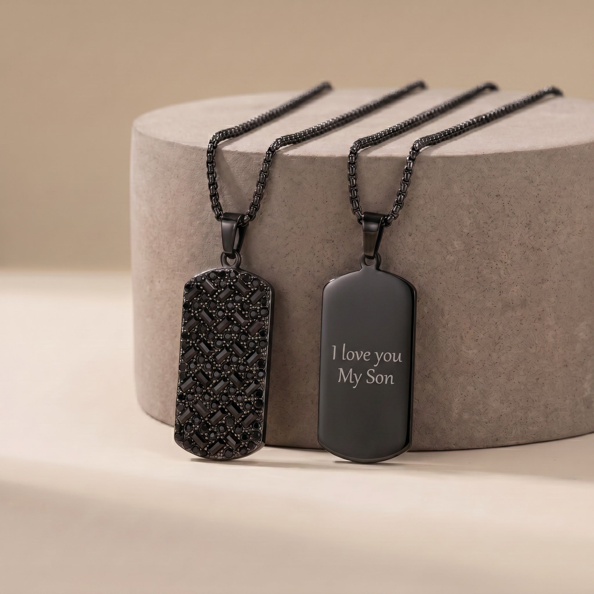 Two black dog tag necklaces on a beige stand with one engraved 'I love you My Son'.
