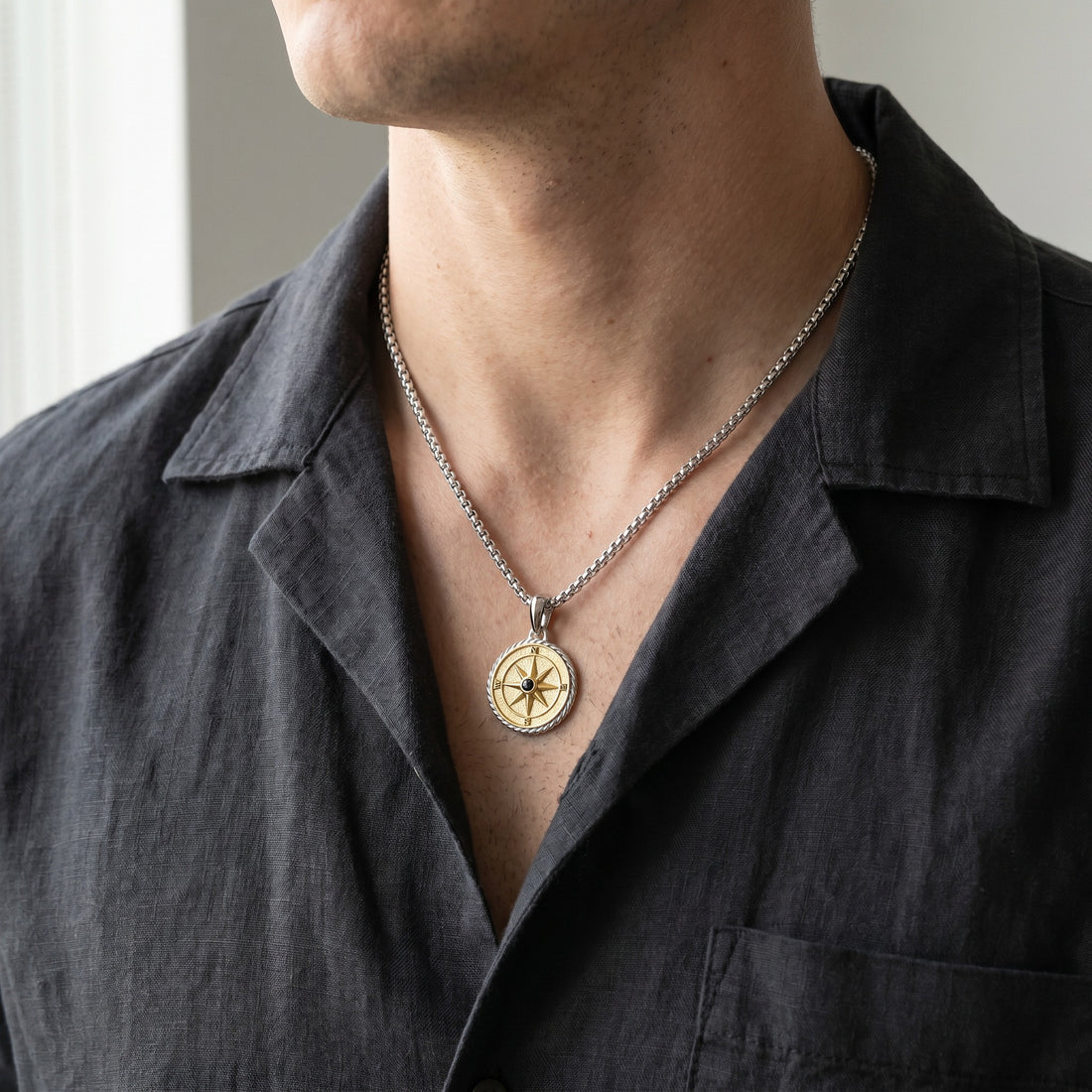 Person wearing a necklace with a compass pendant on a plain background