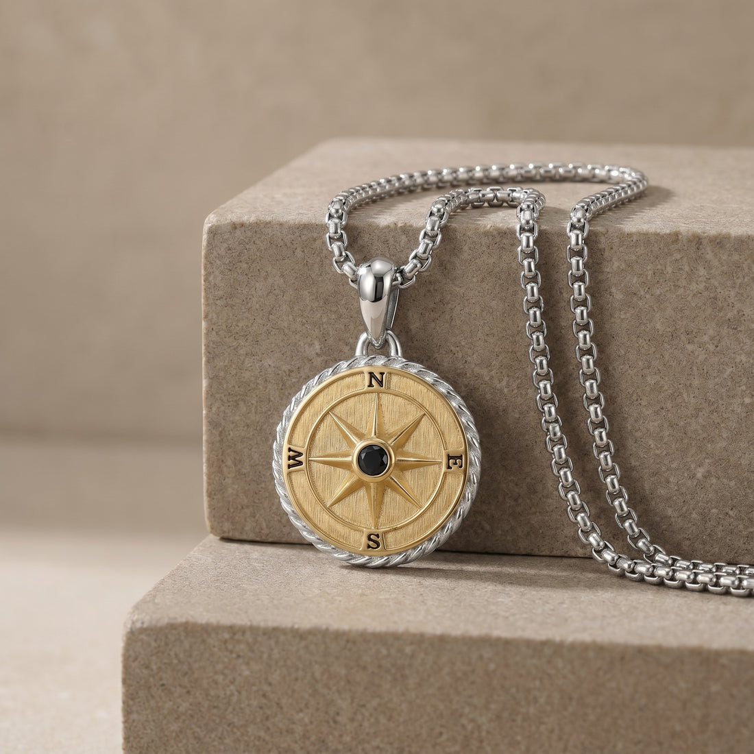 Gold compass pendant necklace on a beige stone surface