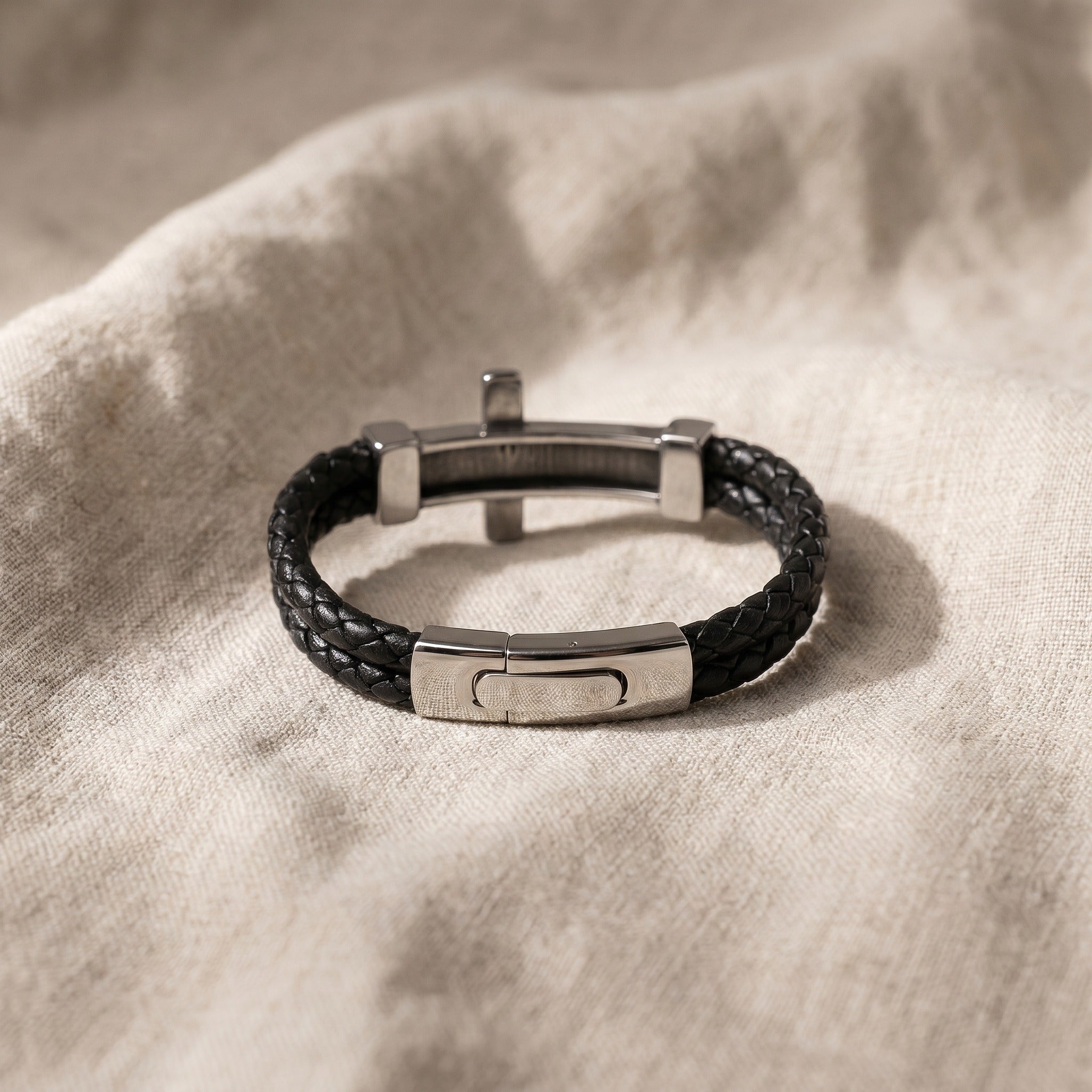 Black leather bracelet with silver metal clasp on a beige fabric background