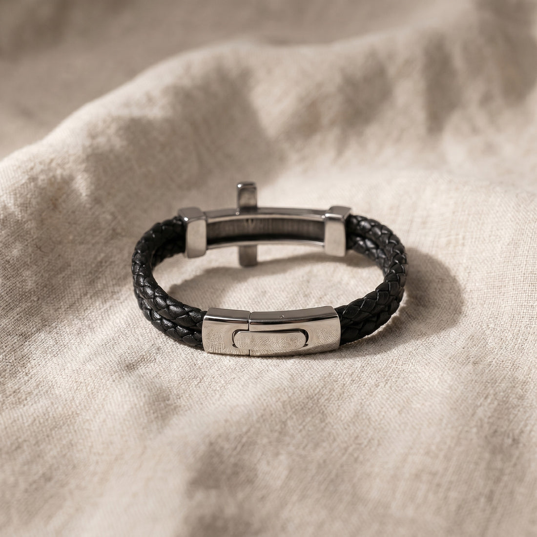 Black leather bracelet with silver metal clasp on a beige fabric background