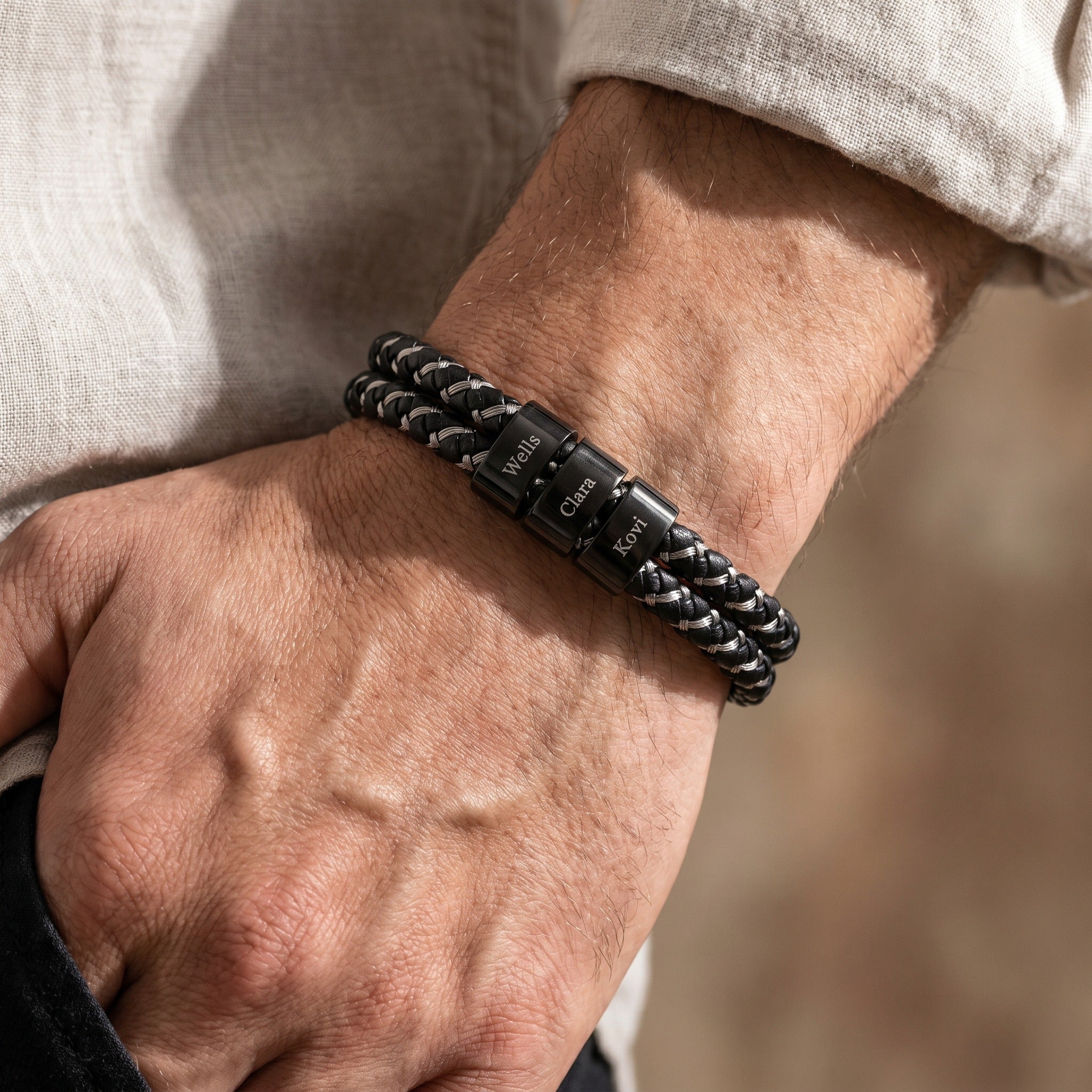 Close-up of a person's wrist wearing a black braided bracelet with engraved text.