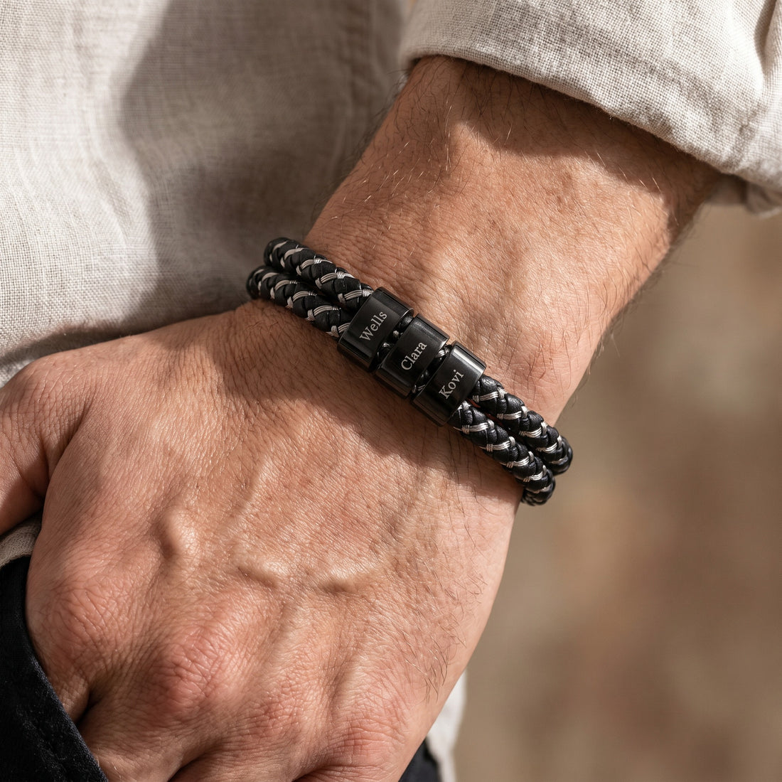 Close-up of a person's wrist wearing a black braided bracelet with engraved text.