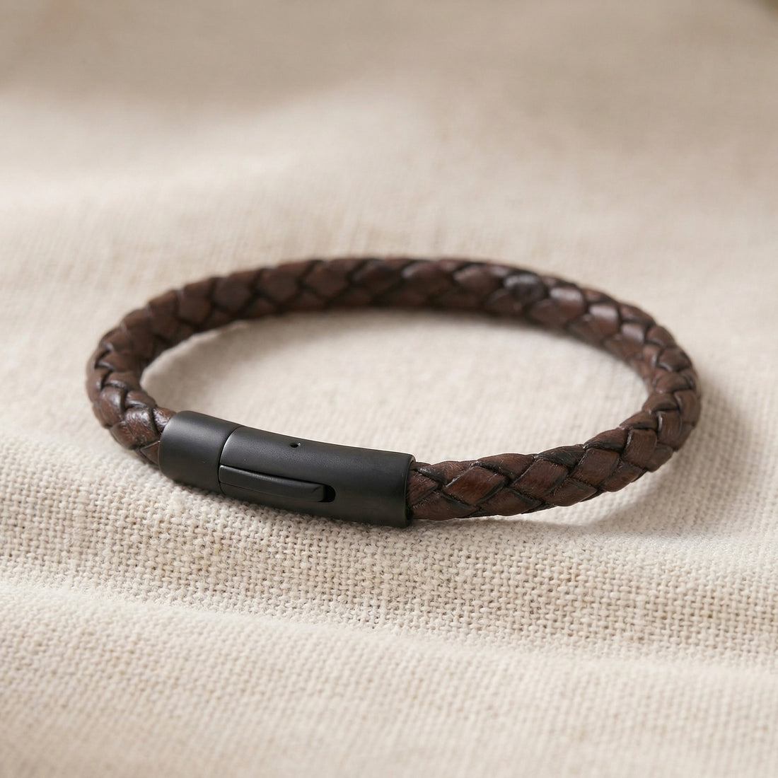Brown braided leather bracelet with a black clasp on a beige fabric background