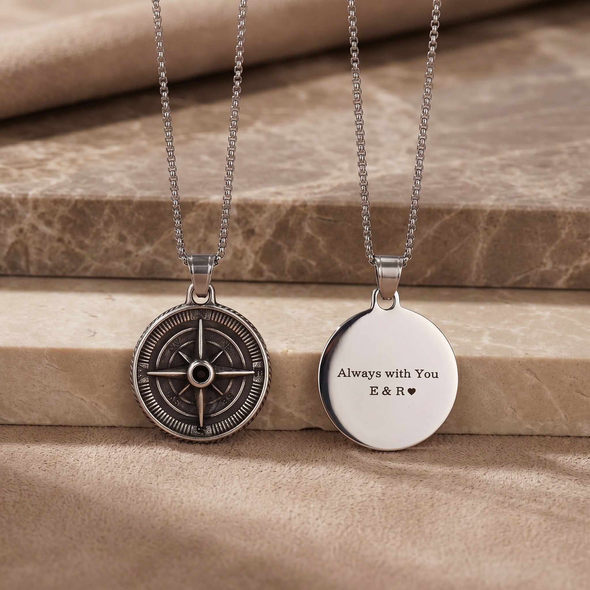 Two necklaces on a wooden surface, one with a compass design and the other with engraved text.