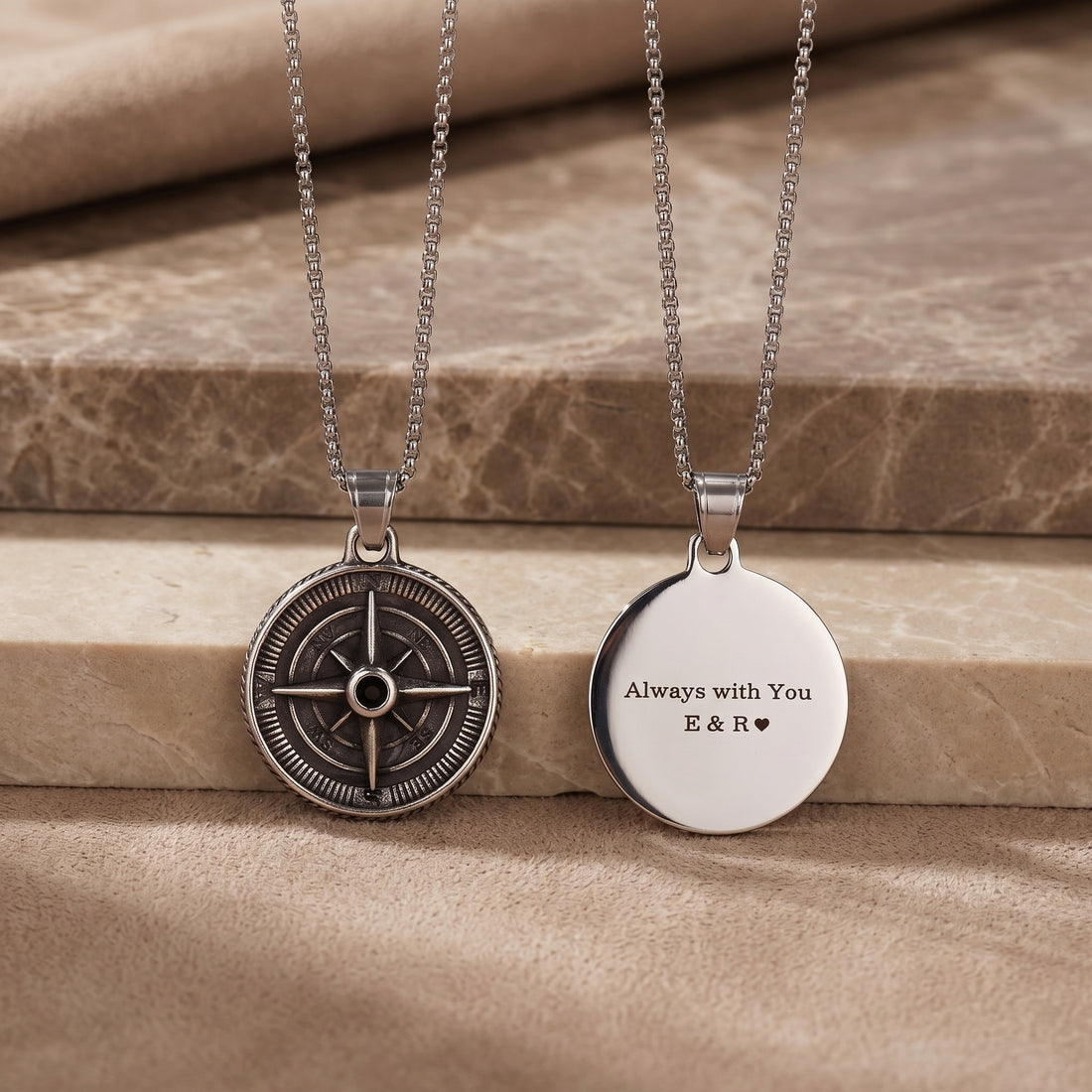 Two necklaces on a wooden surface, one with a compass design and the other with engraved text.