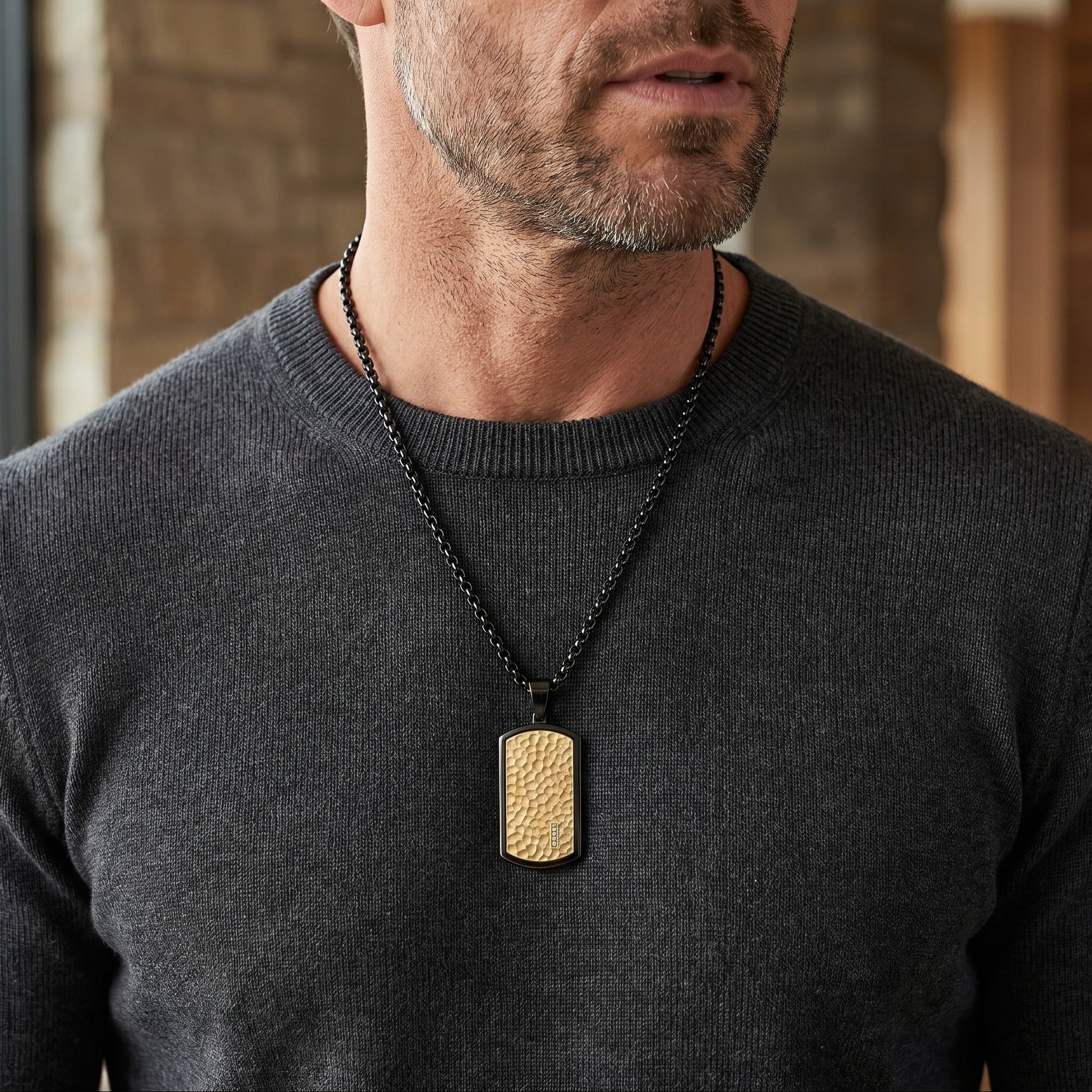 Man wearing a dark gray sweater with a gold pendant necklace.