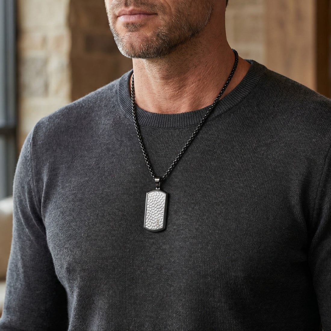 Man wearing a dark gray sweater with a silver dog tag necklace indoors.