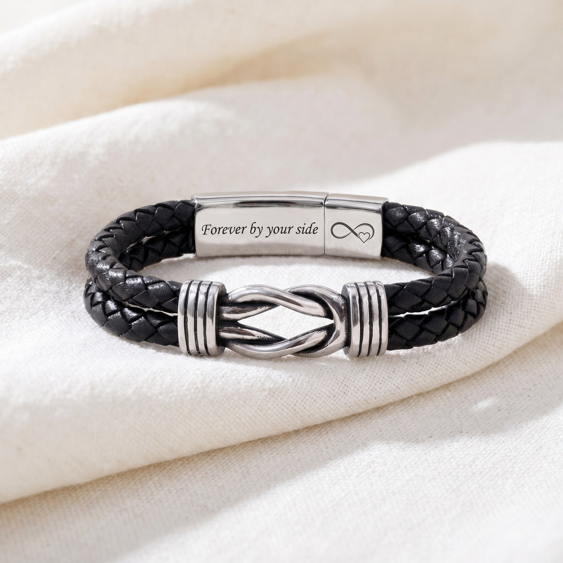 Black braided leather bracelet with silver accents on a white fabric background