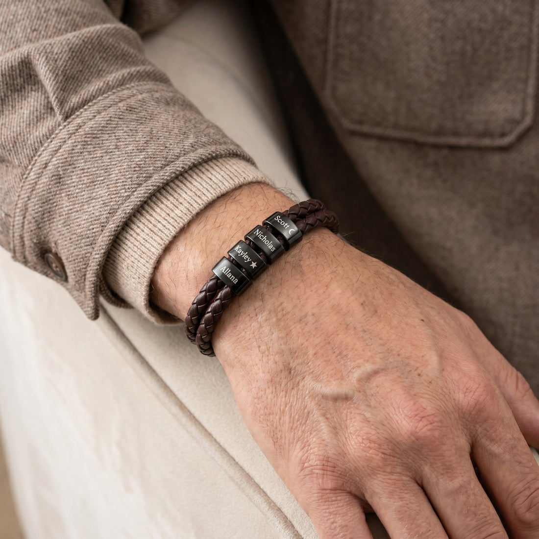 Close-up of a hand wearing a brown leather bracelet with metal clasps on a neutral background