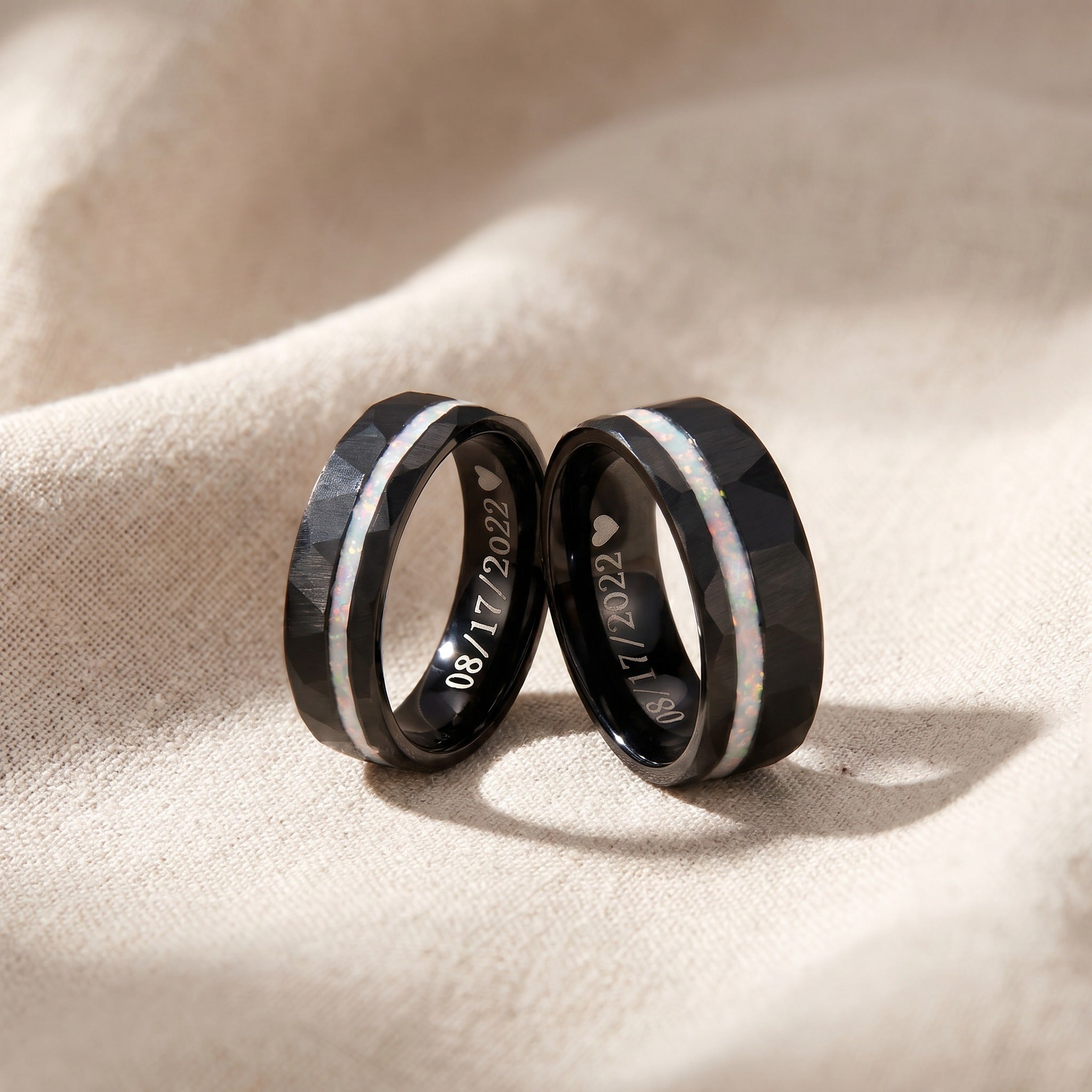 Two black wedding rings with engraved dates on a beige fabric background