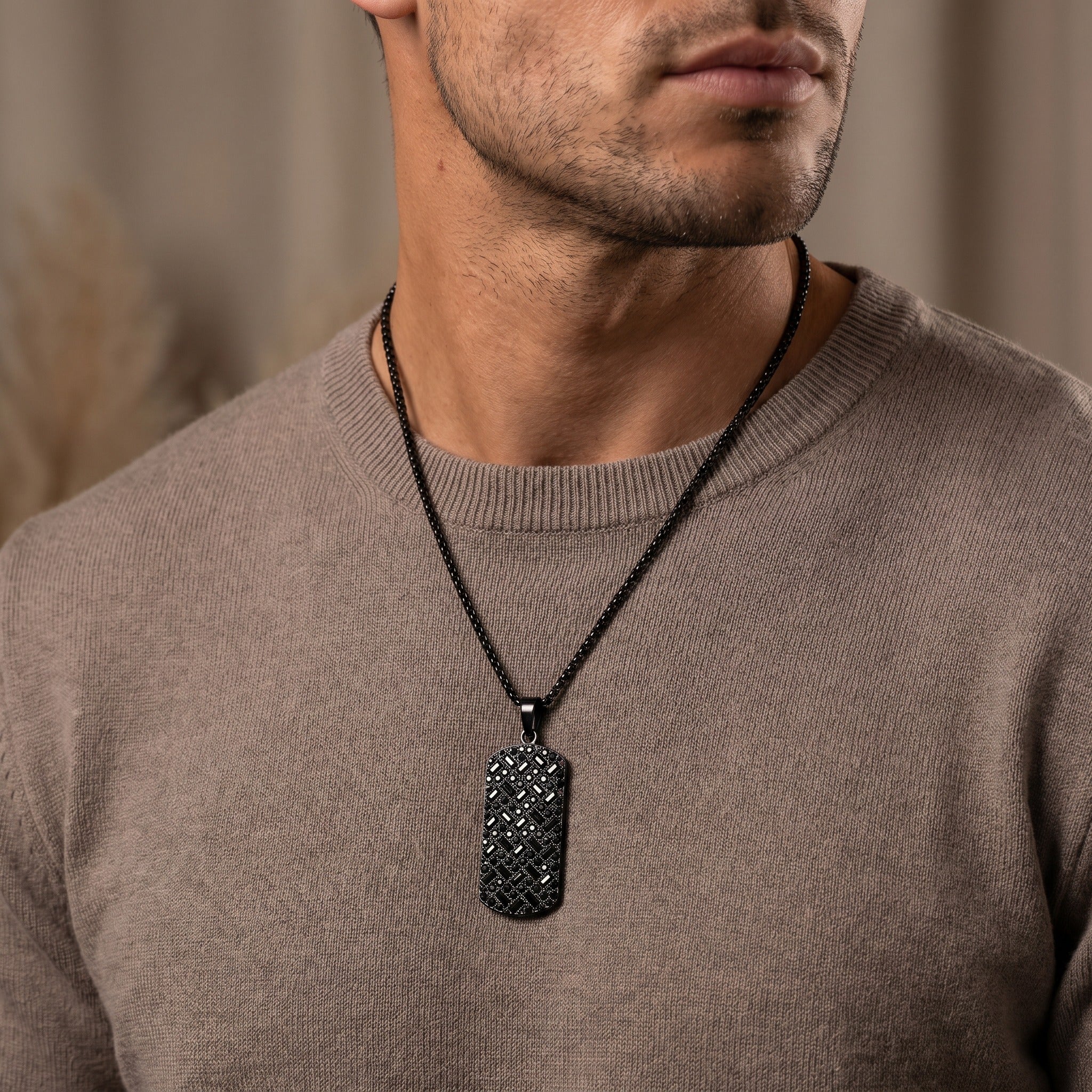 Man wearing a brown sweater with a black necklace featuring a dog tag.