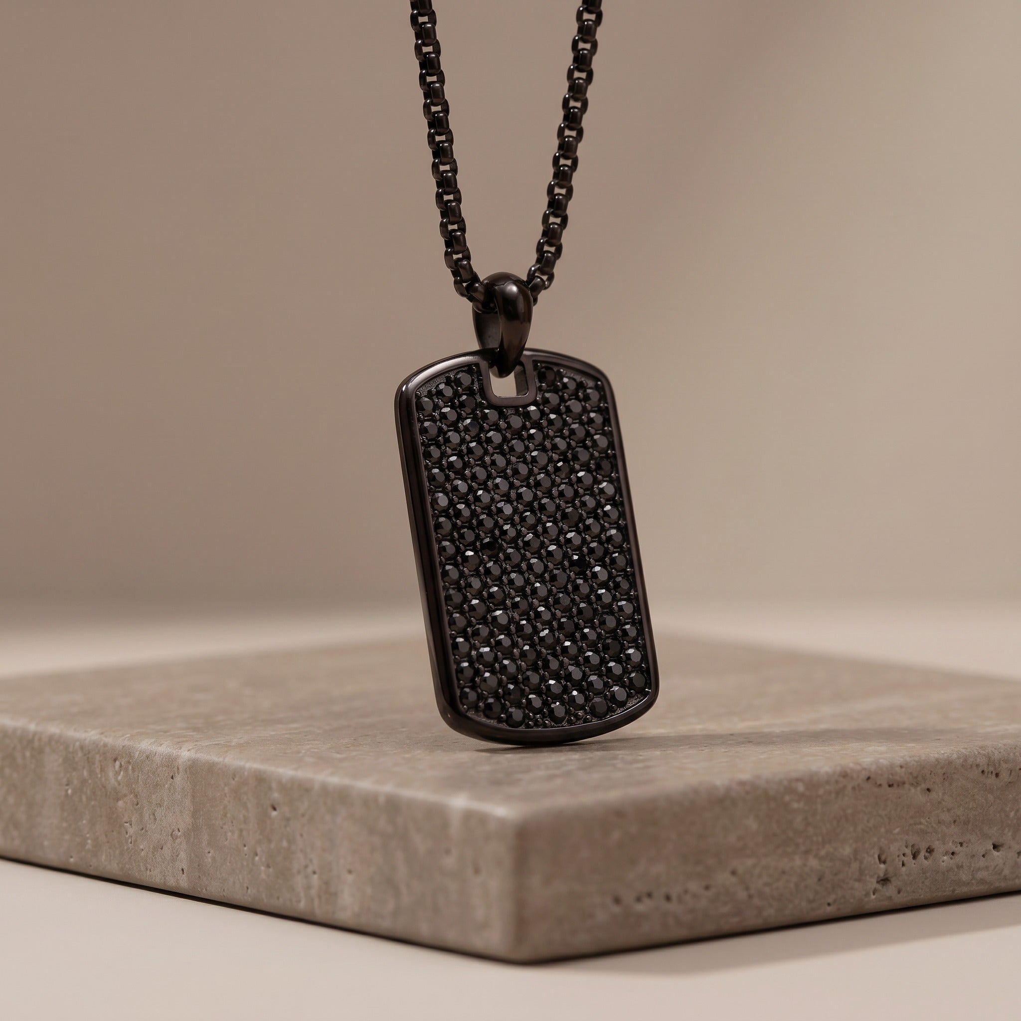 Black textured dog tag necklace on a beige background