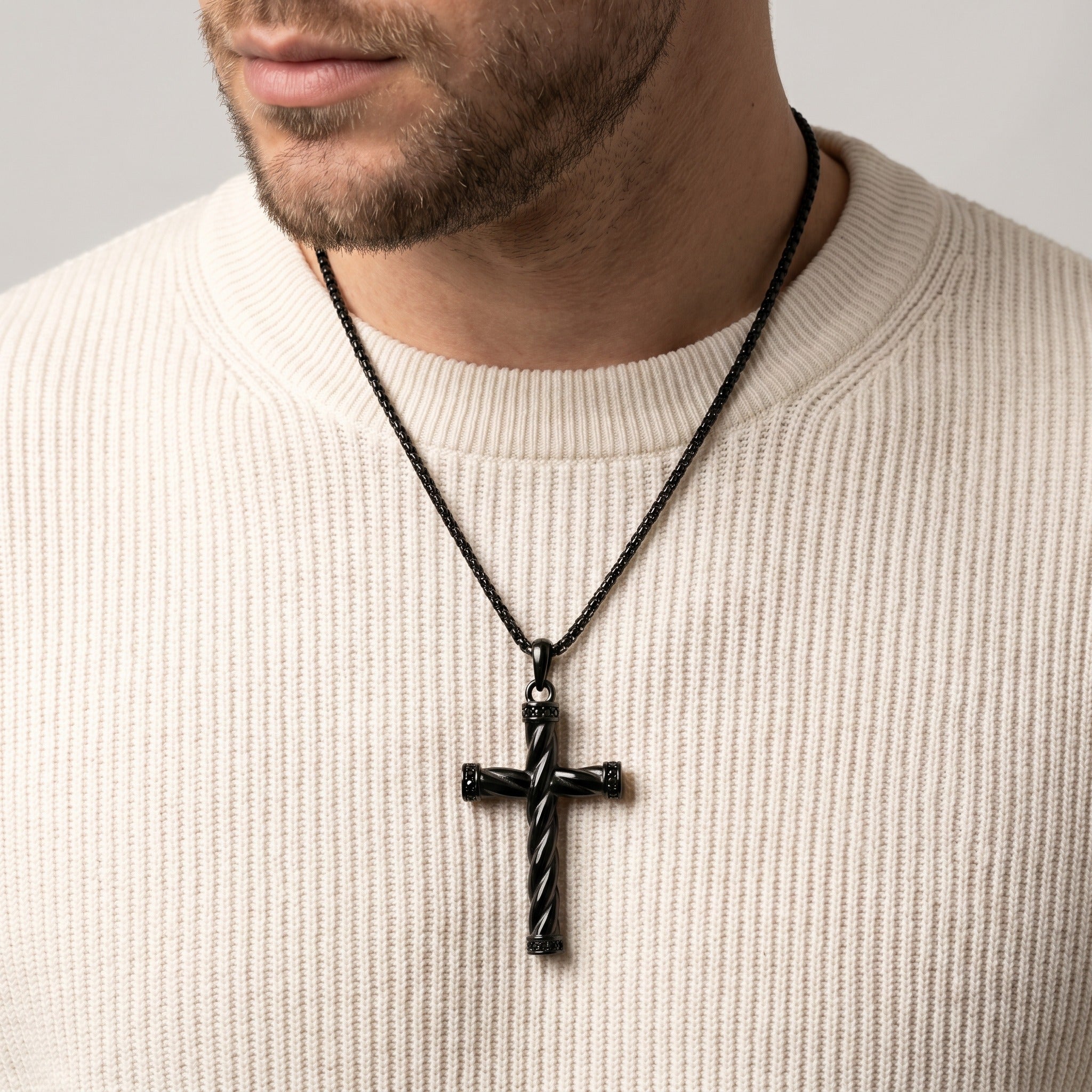 Man wearing a black cross necklace on a plain background
