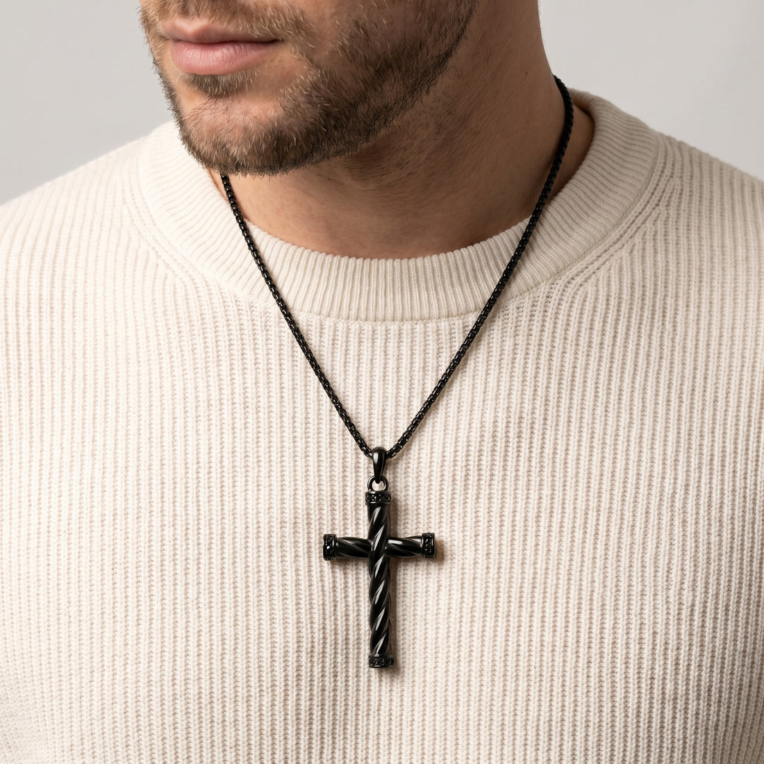 Man wearing a black cross necklace on a plain background