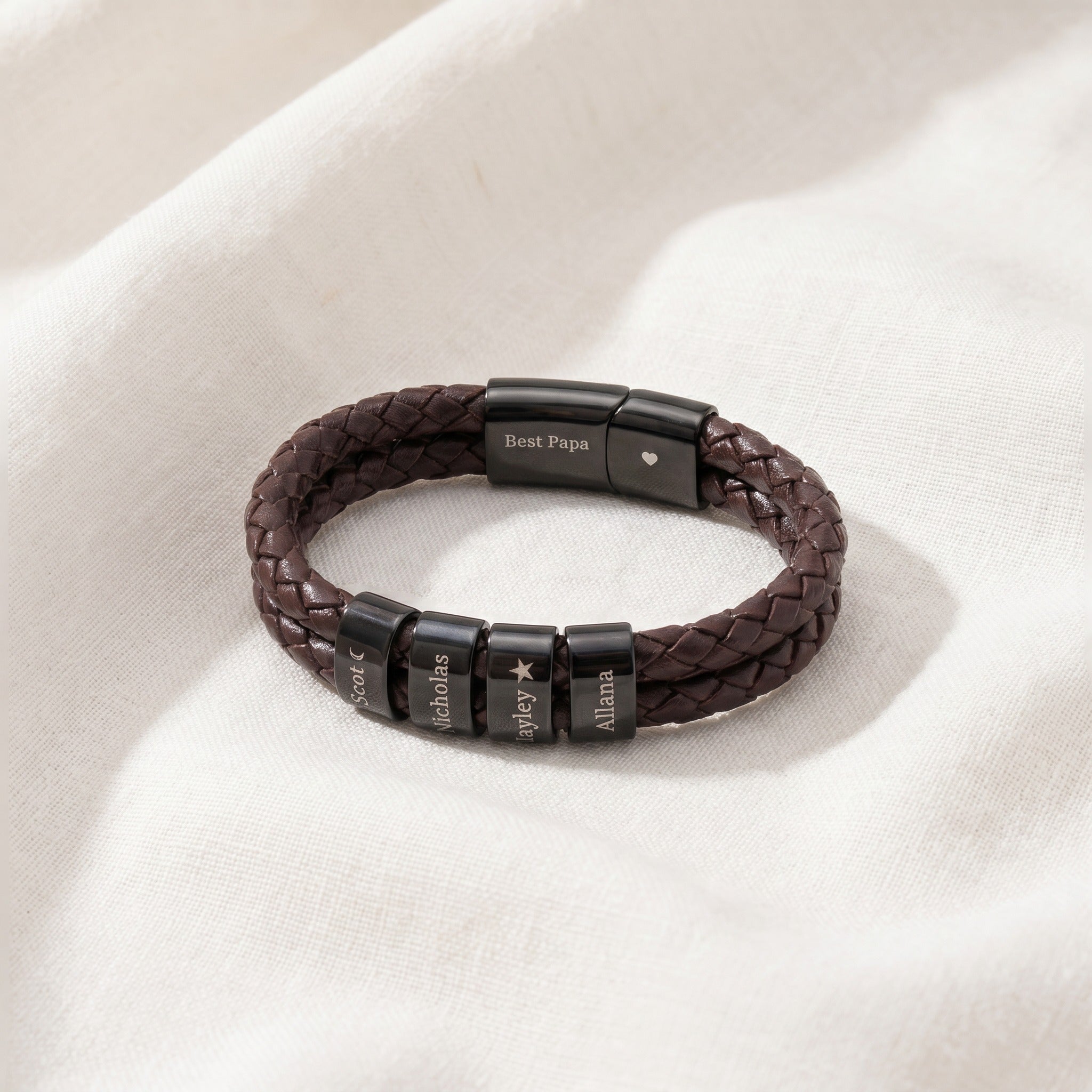 Brown braided leather bracelet with black beads on a beige fabric background