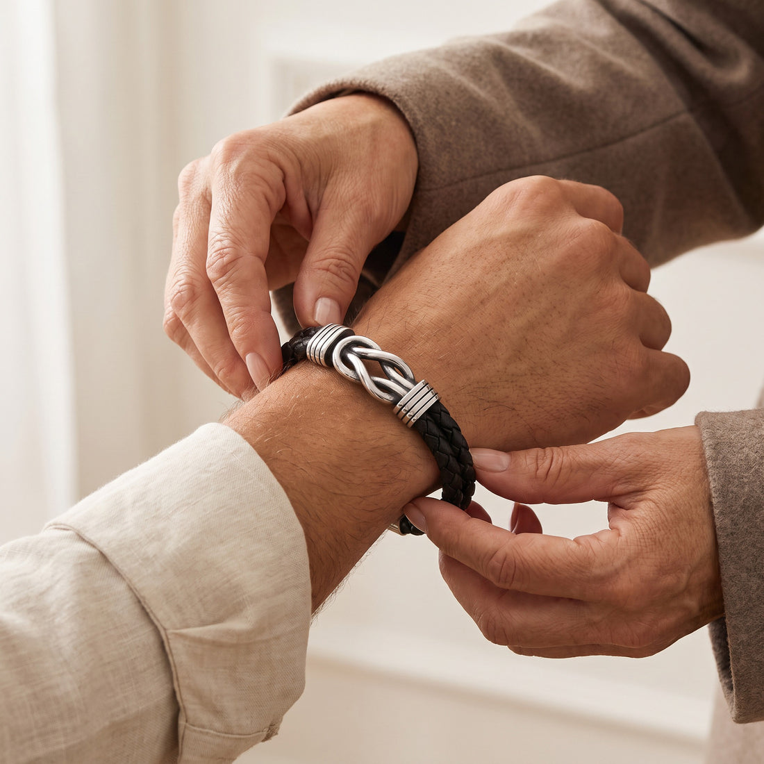 A close-up lifestyle shot of a man adjusting a black braided leather bracelet with a silver-toned knotted metal centerpiece on his wrist.