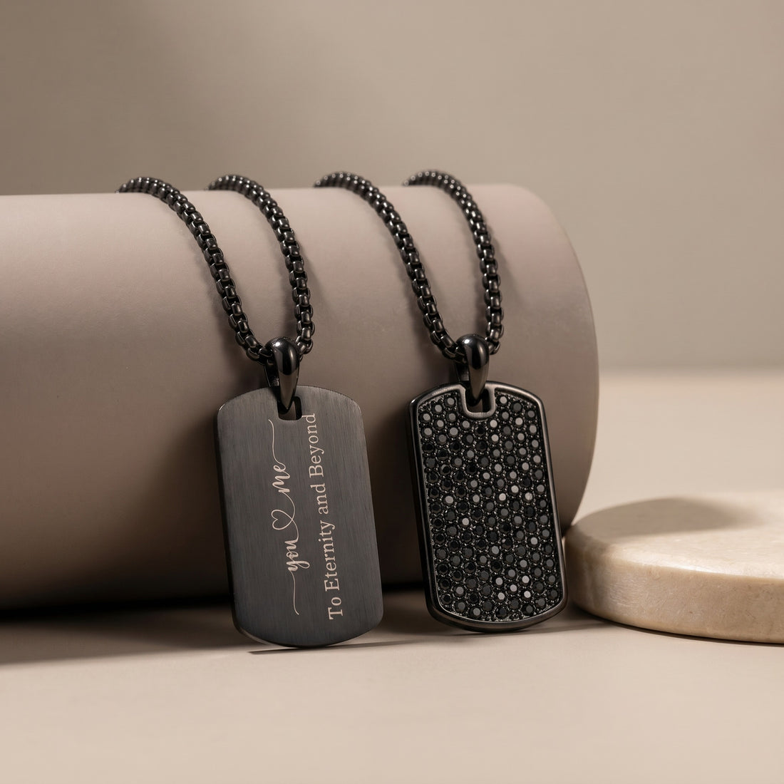 Two black dog tag necklaces on a beige surface