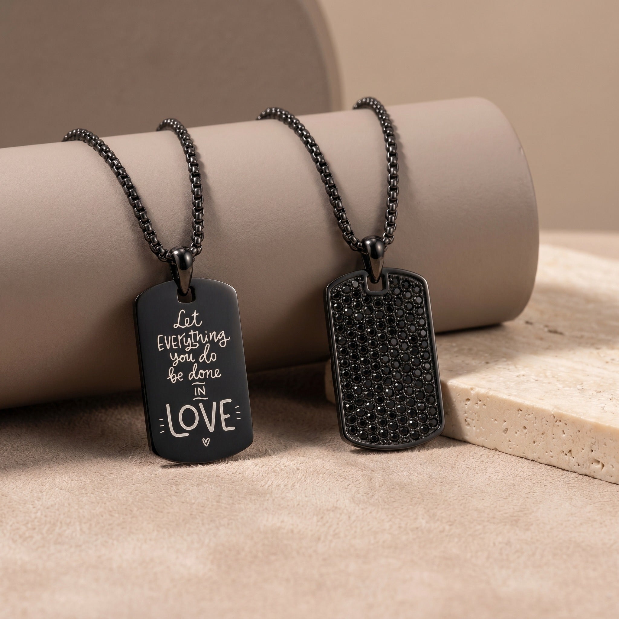 Two black dog tag necklaces on a beige surface