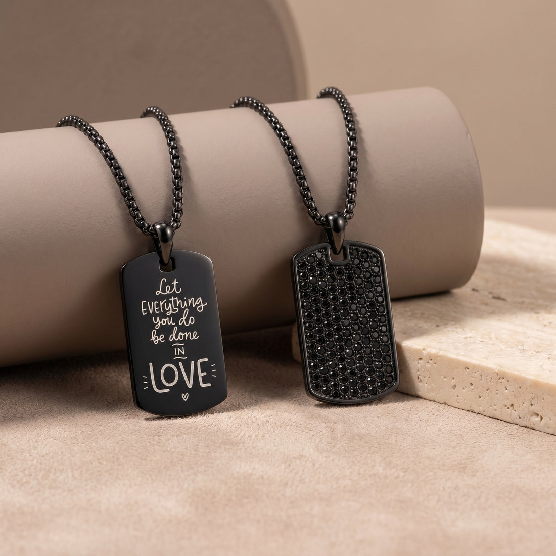 Two black dog tag necklaces on a beige surface