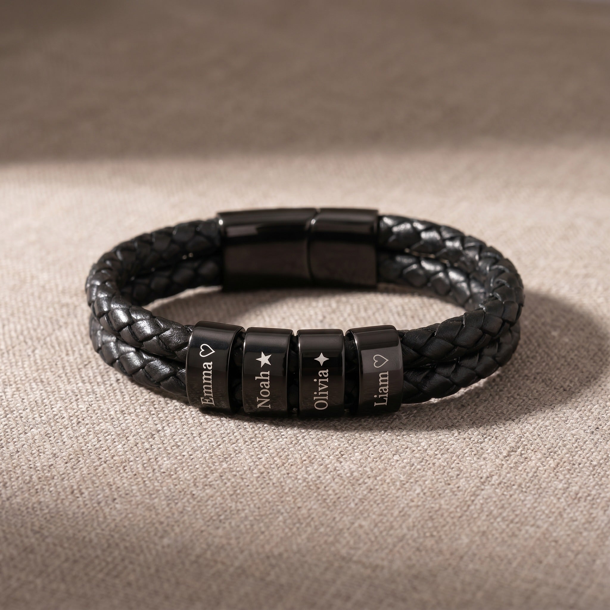 Black braided leather bracelet with engraved beads on a beige fabric background