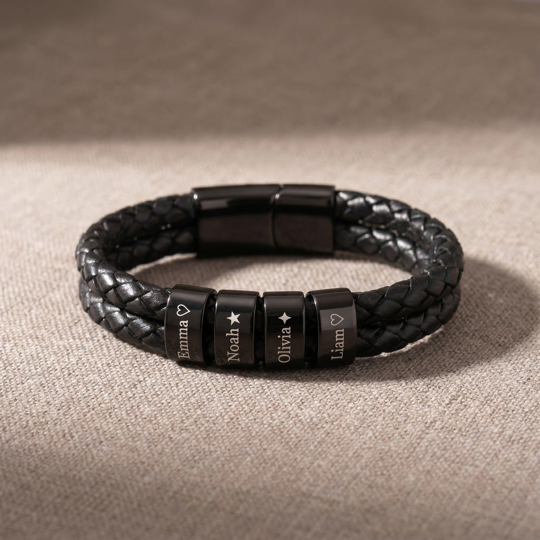 Black braided leather bracelet with engraved beads on a beige fabric background