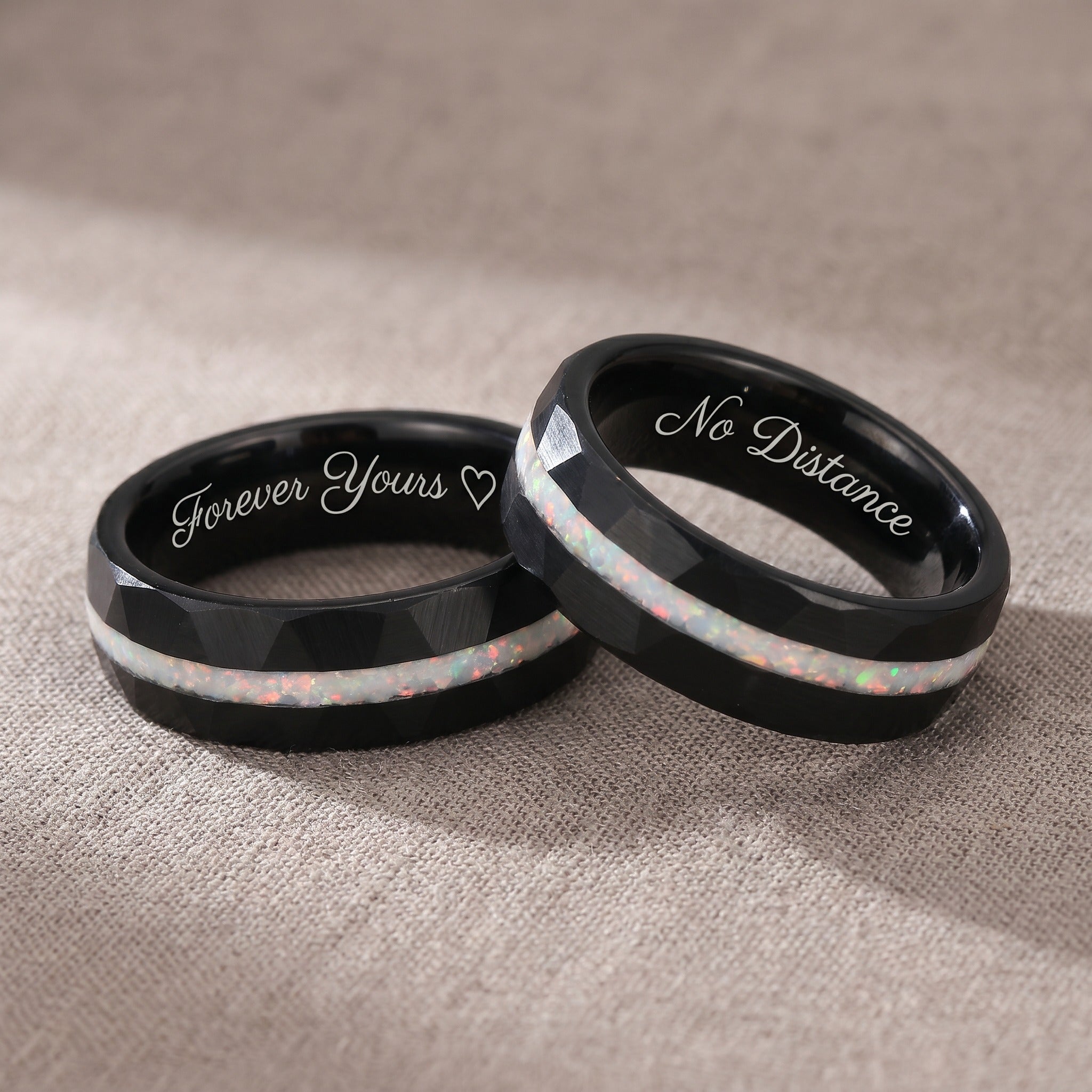 Two black rings with engraved text on a beige fabric background