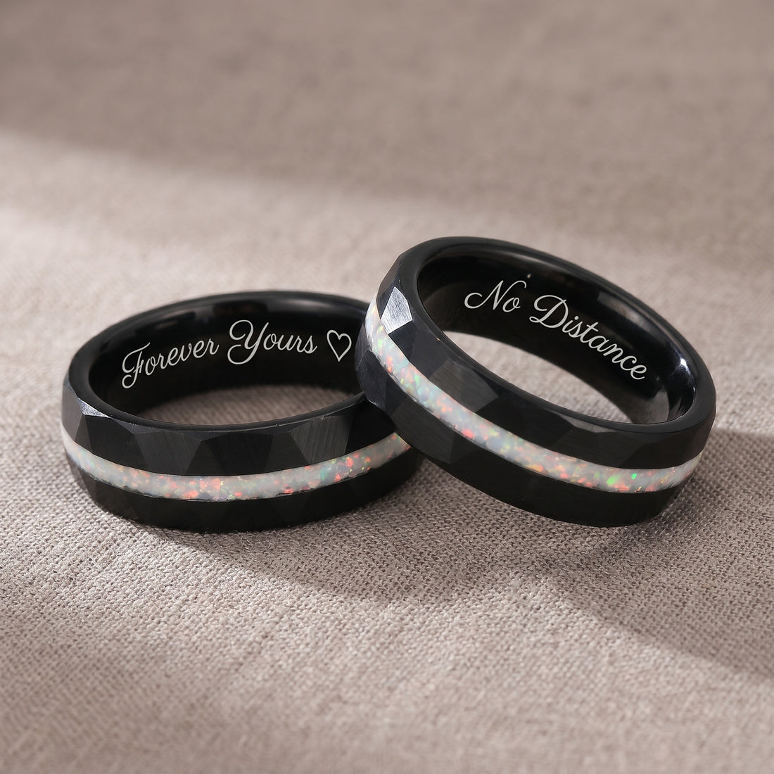 Two black rings with engraved text on a beige fabric background