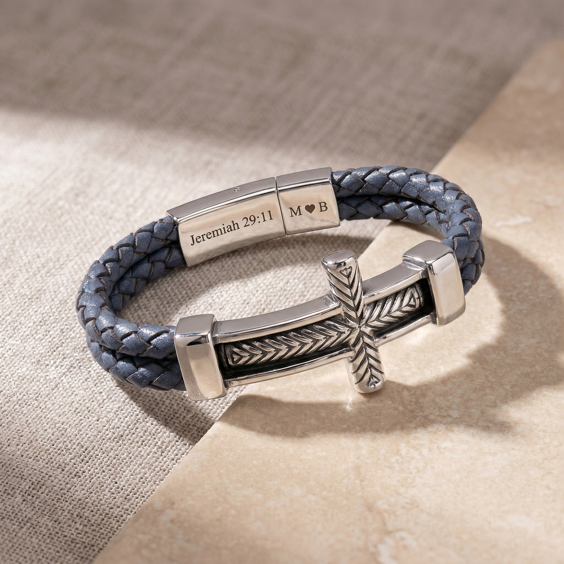 Blue braided leather bracelet with silver metal clasp and cross charm on beige fabric background
