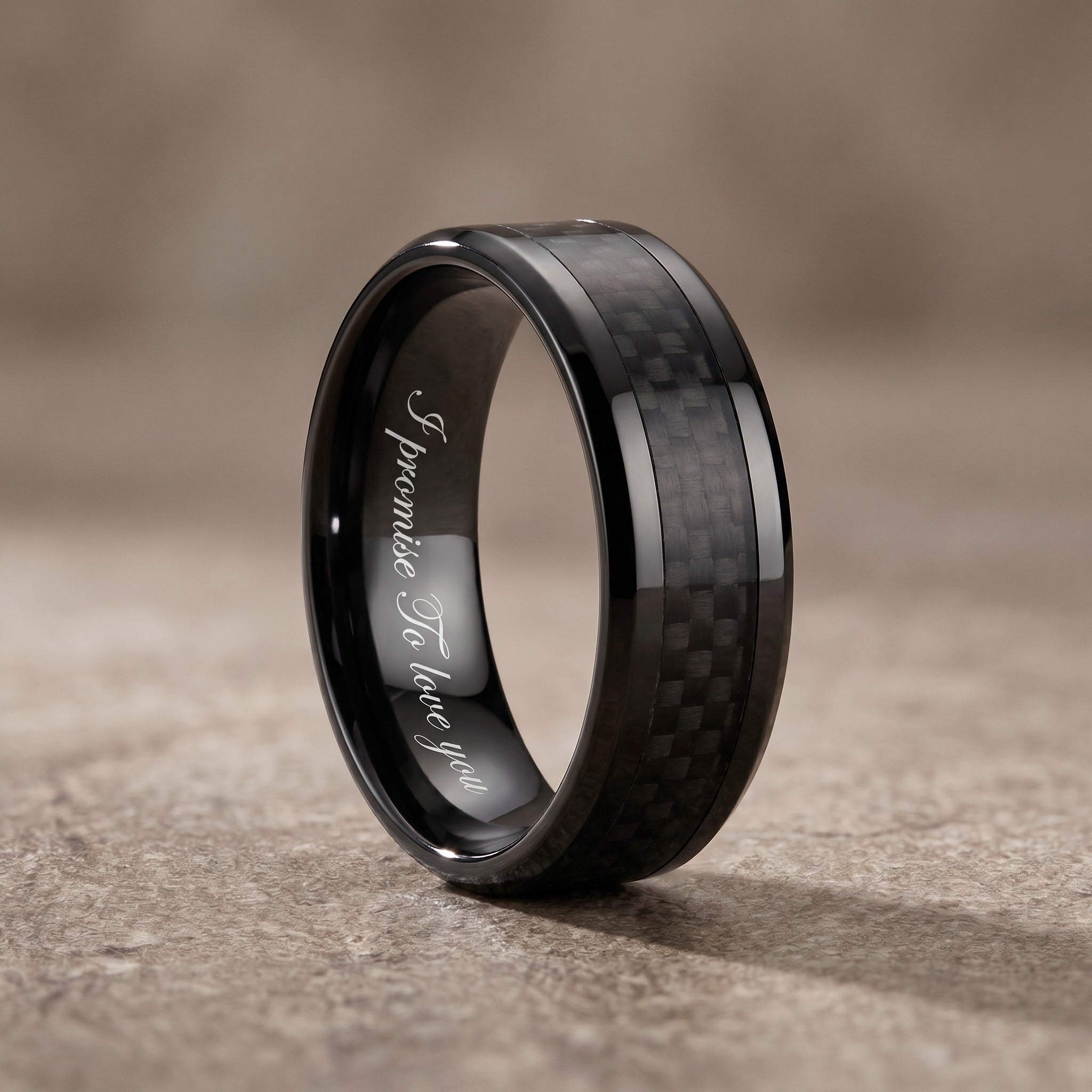 Black ring with carbon fiber inlay and engraved text on a textured surface