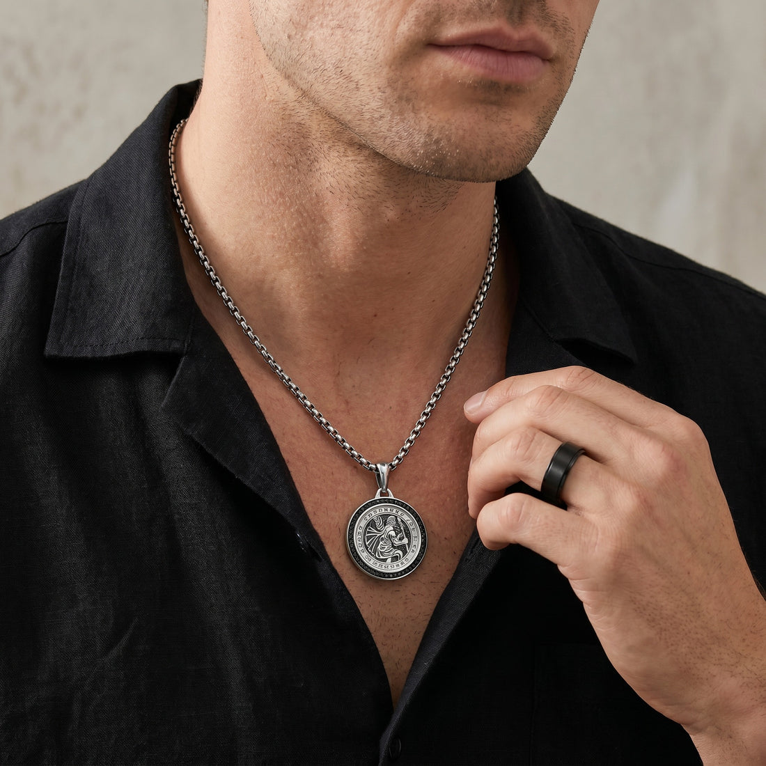 Man wearing a black shirt with a silver necklace featuring a pendant.