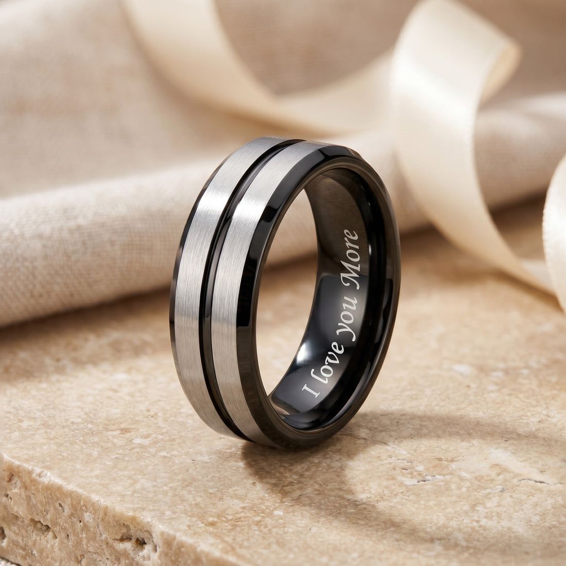 Silver and black ring with 'I Love You More' engraving on a beige stone surface